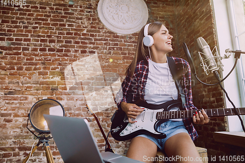 Image of Woman recording music, playing guitar and singing at home