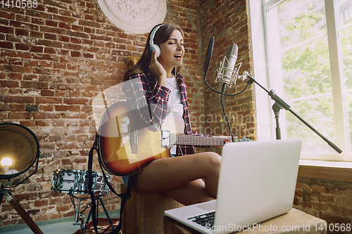 Image of Woman recording music, playing guitar and singing at home