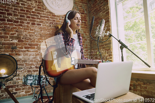 Image of Woman recording music, playing guitar and singing at home