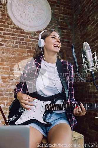 Image of Woman recording music, playing guitar and singing at home