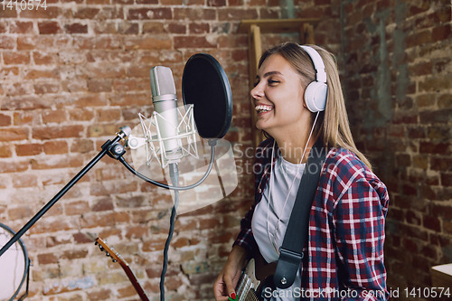Image of Woman recording music, playing guitar and singing at home