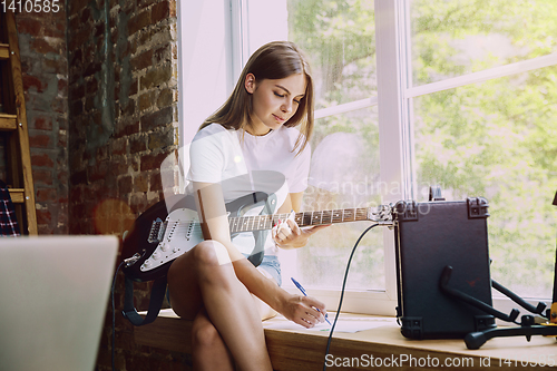 Image of Woman recording music, playing guitar and singing at home