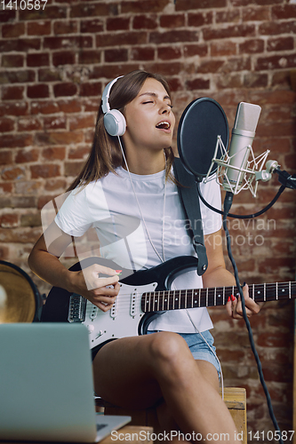 Image of Woman recording music, playing guitar and singing at home