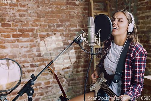 Image of Woman recording music, playing guitar and singing at home