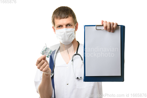 Image of The doctor shows a tablet with a white sheet of paper in the frame, holds medicines in the other hand