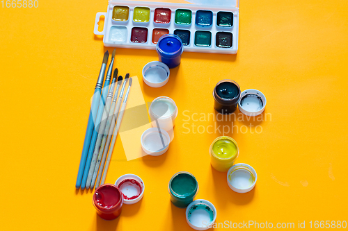 Image of Brushes, jars of gouache and watercolor paints lie on a yellow background