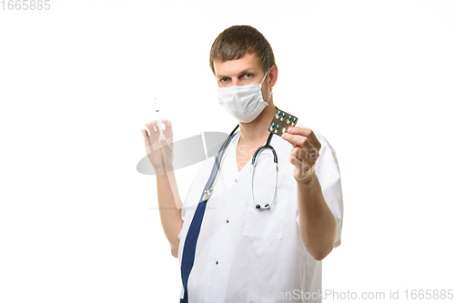 Image of A male doctor holds a syringe with a medicine in one hand and a pill in the other hand