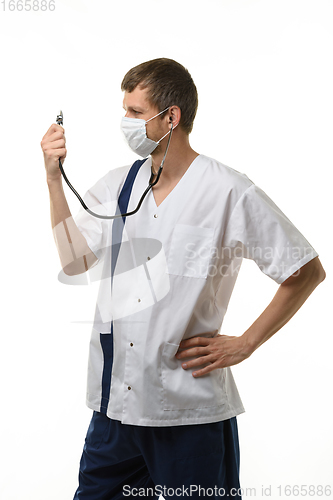 Image of Doctor in a mask looks at a phonendoscope dressed on himself