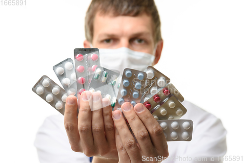 Image of A man in a medical mask sips a fan of medicines into the frame, focusing on medicines