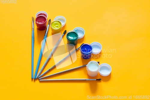 Image of Brushes and jars of gouache are laid out on a yellow background