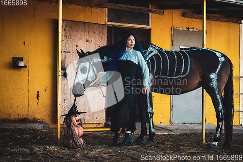 Image of A girl dressed as a witch on a farm, a horse with a skeleton is drawn next to it, as well as three pumpkins in the shape of an evil man