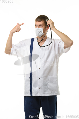Image of Masked doctor using a phonendoscope listens to his head, with the other hand making a pistol gesture points to his head, isolated on white background