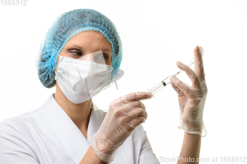 Image of Nurse in mask and gloves draws medicine with a syringe from an ampoule