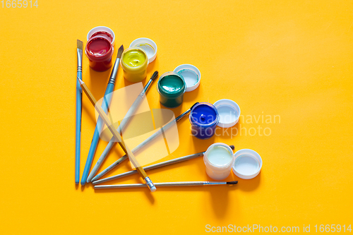 Image of Brushes and one pencil are laid out on the table, jars of gouache are nearby