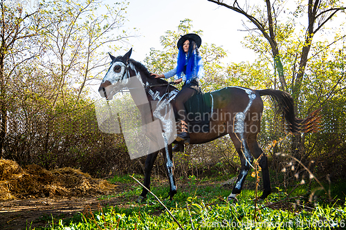 Image of A girl dressed as a witch rides a horse on which a skeleton is painted in white paint