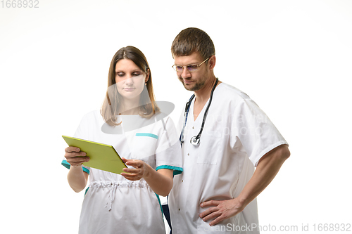 Image of Doctor and nurse discussing the patient\'s tests, looking thoughtfully into the screen of a tablet computer