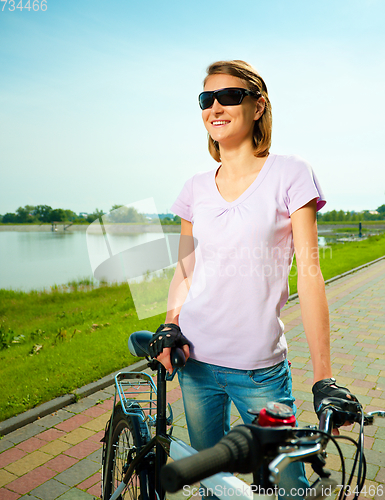 Image of Young woman is standing behind bicycle