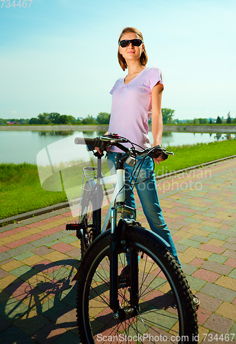 Image of Young woman is standing behind bicycle