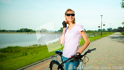 Image of Young woman is standing behind bicycle
