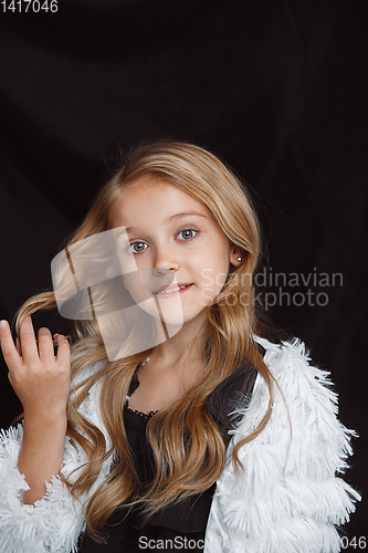 Image of Little smiling girl posing in white outfit on black studio background