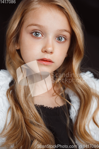 Image of Little smiling girl posing in white outfit on black studio background