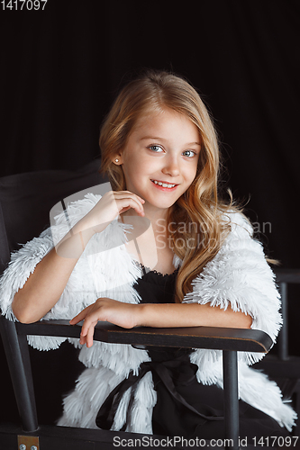 Image of Little smiling girl posing in white outfit on black studio background