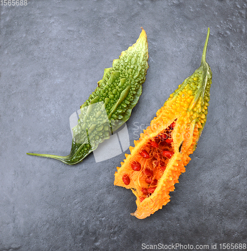 Image of Two bitter melons - with green ridged skin and overripe orange f