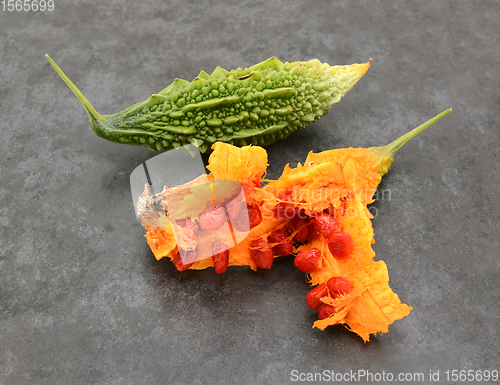 Image of Green bitter gourd and overripe orange fruit, split apart