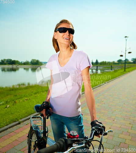 Image of Young woman is standing behind bicycle