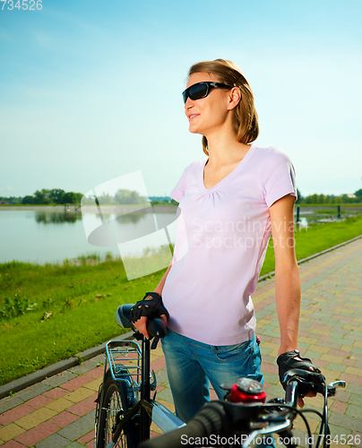 Image of Young woman is standing behind bicycle