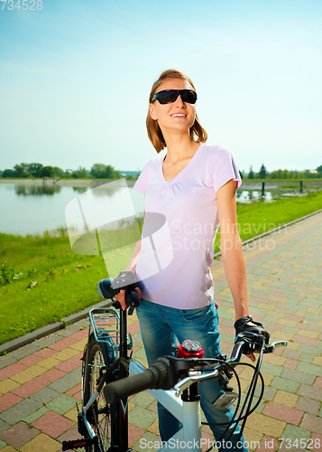 Image of Young woman is standing behind bicycle