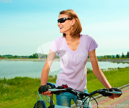 Image of Young woman is standing behind bicycle