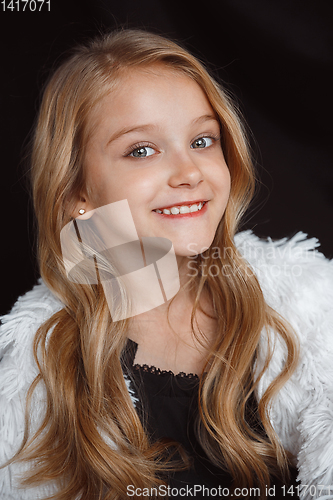 Image of Little smiling girl posing in white outfit on black studio background