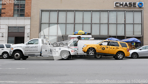 Image of Broken down yellow taxi cab being towed away by a recovery vehic