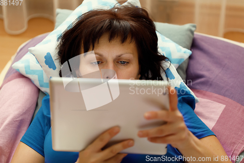 Image of Middle age woman resting in bed with tablet