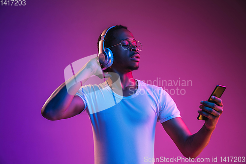Image of Young african-american man\'s listening to music in neon light