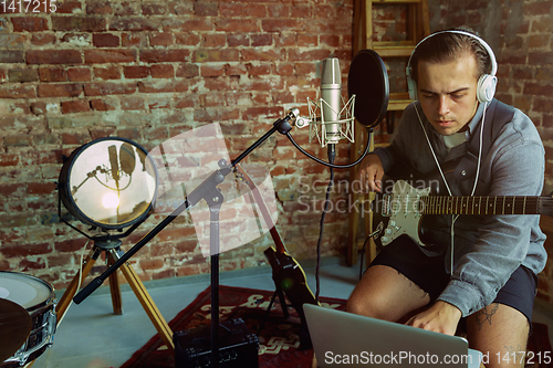 Image of Young man recording music, playing guitar and singing at home