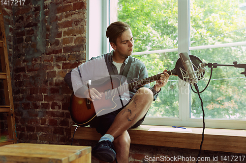 Image of Young man recording music, playing guitar and singing at home