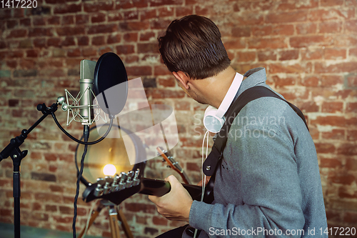 Image of Young man recording music, playing guitar and singing at home