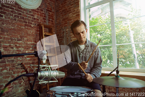 Image of Young man recording music, playing drums and singing at home