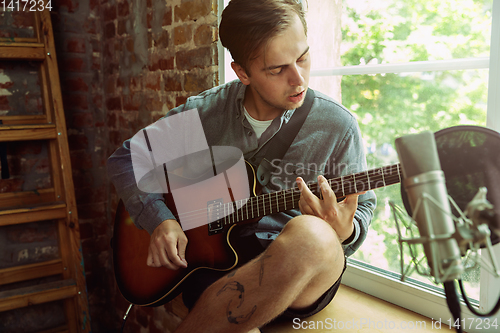 Image of Young man recording music, playing guitar and singing at home