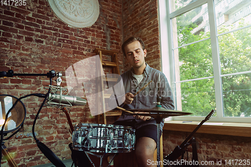 Image of Young man recording music, playing drums and singing at home