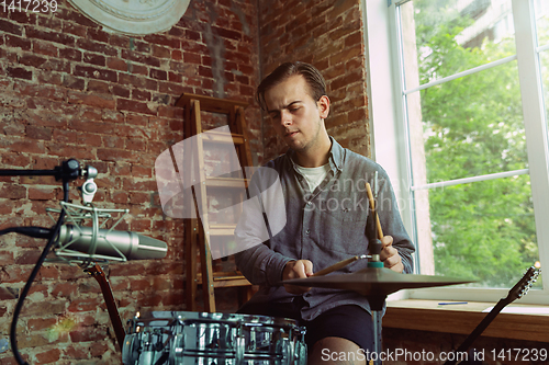 Image of Young man recording music, playing drums and singing at home