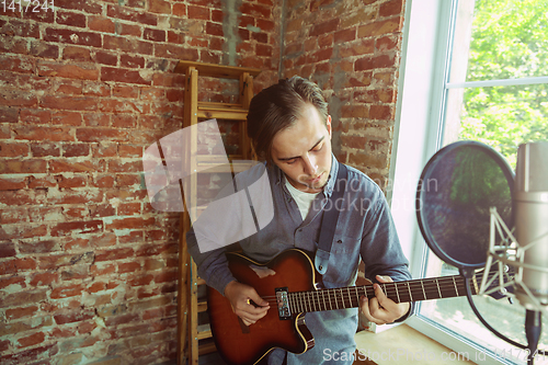 Image of Young man recording music, playing guitar and singing at home