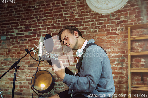 Image of Young man recording music, playing guitar and singing at home