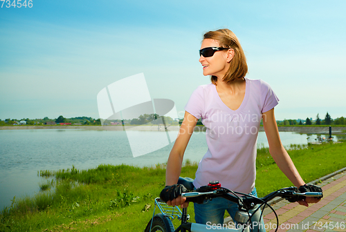 Image of Young woman is standing behind bicycle