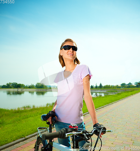Image of Young woman is standing behind bicycle