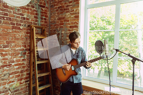 Image of Young man recording music, playing guitar and singing at home