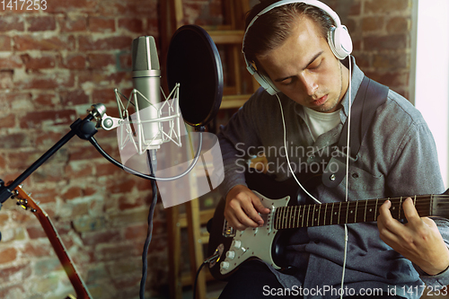 Image of Young man recording music, playing guitar and singing at home