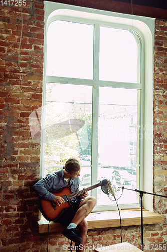 Image of Young man recording music, playing guitar and singing at home